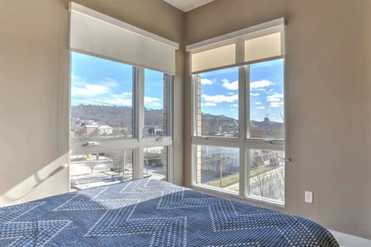 A serene bedroom with a bed featuring blue patterned bedding, large windows that offer a sweeping mountain view, and natural light filling the room. The decor is calming, with minimalist touches and a tranquil atmosphere.