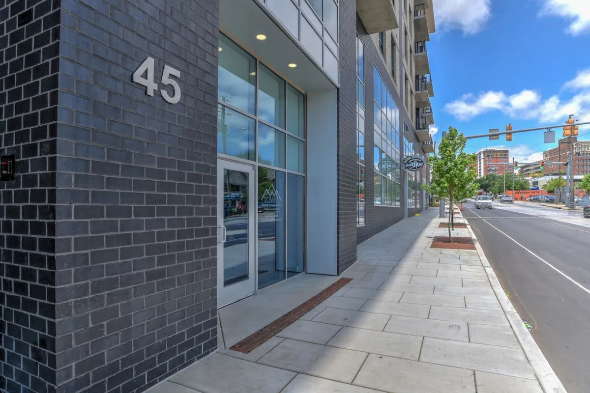 This exterior image displays the building’s facade, marked by the number 45, with large glass windows and an inviting sidewalk. The modern appearance reflects a secure, urban residence in a bustling location.
