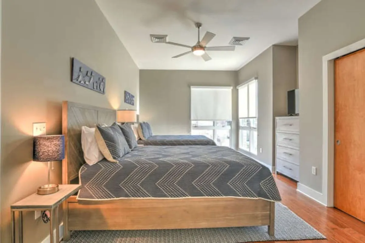 This image features two beds with decorative wall art above them, a nightstand with a lamp, and a window allowing natural light to stream in. The beds appear plush and inviting, and the space feels warm and comfortable, suitable for either family or friends sharing a room.