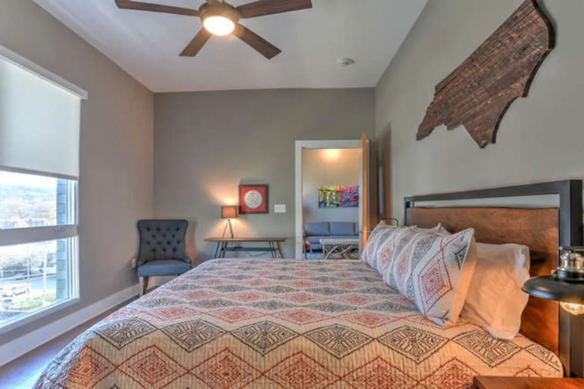A cozy bedroom scene featuring a patterned bed, comfortable armchair, decorative wall art, and a softly lit lamp. This space feels like an inviting retreat for friends or couples to relax and unwind between city outings.